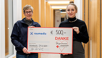 Elke Kiener, representing the Herzenswunschmobil, accepts the symbolic cheque from Lisa Schwiersch, Head of Marketing & Communication at RAUMEDIC AG.